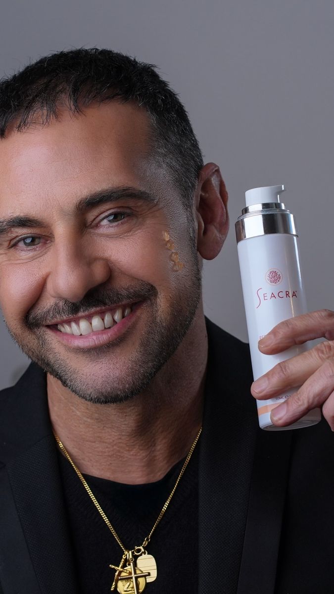Studio skincare campaign portrait of a smiling man holding a Seacra bottle with gel on his cheek