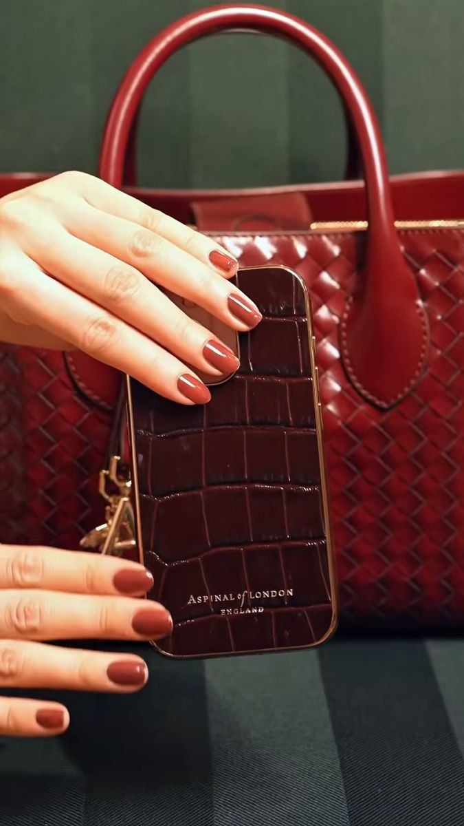 A burgundy croc phone case going into a burgundy woven bag, Aspinal of London